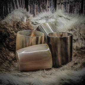 Fyra whiskysglas i polerad horn med glatt finish, arrangerade på pelskudde med trästöd