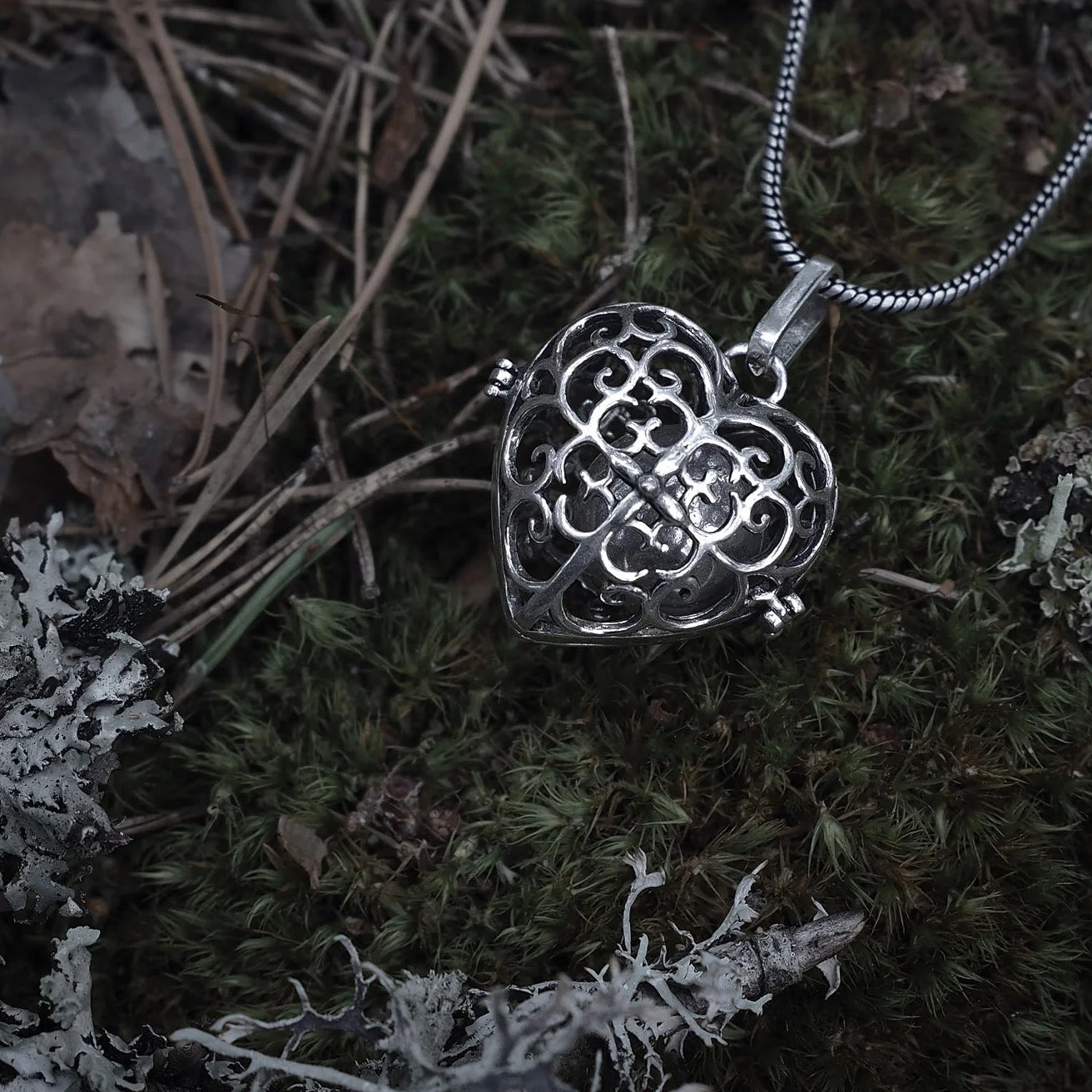Två berlocker med solspiralmönster - en i silverpläterad finish och en i mässing. Båda visar samma intrika spiraldesign utskärd genom den sfäriska bärlocken, fotograferad från sidan för att visa mönstrets komplexitet.