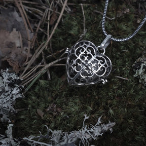 Två berlocker med solspiralmönster - en i silverpläterad finish och en i mässing. Båda visar samma intrika spiraldesign utskärd genom den sfäriska bärlocken, fotograferad från sidan för att visa mönstrets komplexitet.