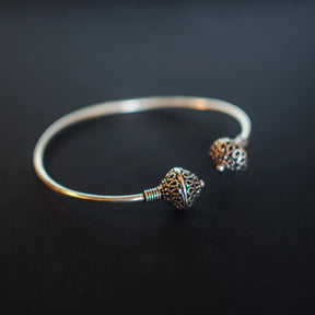 Silverpläterad mässingarmband med två pärlor på mörkbakgrund. Öppen armring med två graverade pärlor i mässing som visar vikingatida motiv. Polerad finish med varma guldtoner. Tråd-lindningar vid anslutningspunkterna demonstrerar traditionell metallteknik.