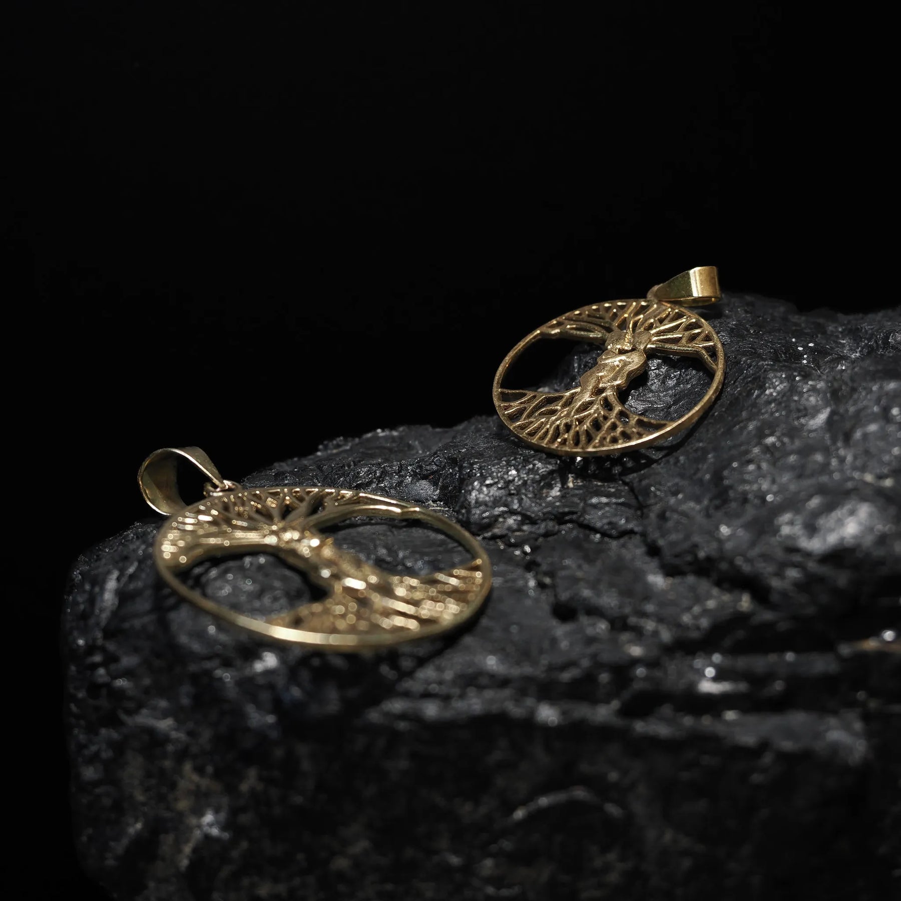 Stor träd-amulett i mässing/guld fotograferad på mörkgrå sten, visar Yggdrasil med synliga grenar och rötter.