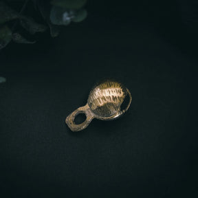 Närbild av mässingbjällra Rispig-variant som visar detaljer av fint graverat radialt mönster på kullrig yta