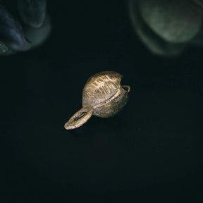 35mm mässingklocka med Rispig (ripplad) ytfinish. Linjära åsar bildar framträdande vågmönster. Sfärisk form med metallisk glans. Naturlig växtbakgrund visar artisanal hantverksstil.