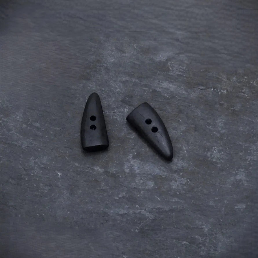 En mörk hornknapp med naturlig färg och kornmönster. Kugel-/spetsig form med två hål för sömnad. Visar autentisk hornmaterial.