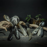 Bestickset i organiskt horn med matskelar, teskelar och smörkniv, arrangerade på rustik träyta med växter