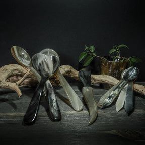 Bestickset i organiskt horn med matskelar, teskelar och smörkniv, arrangerade på rustik träyta med växter