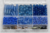 Bead box organizer containing blue glass beads in six different shades and sizes ranging from 6mm to larger faceted stones, with metal findings in bottom compartment