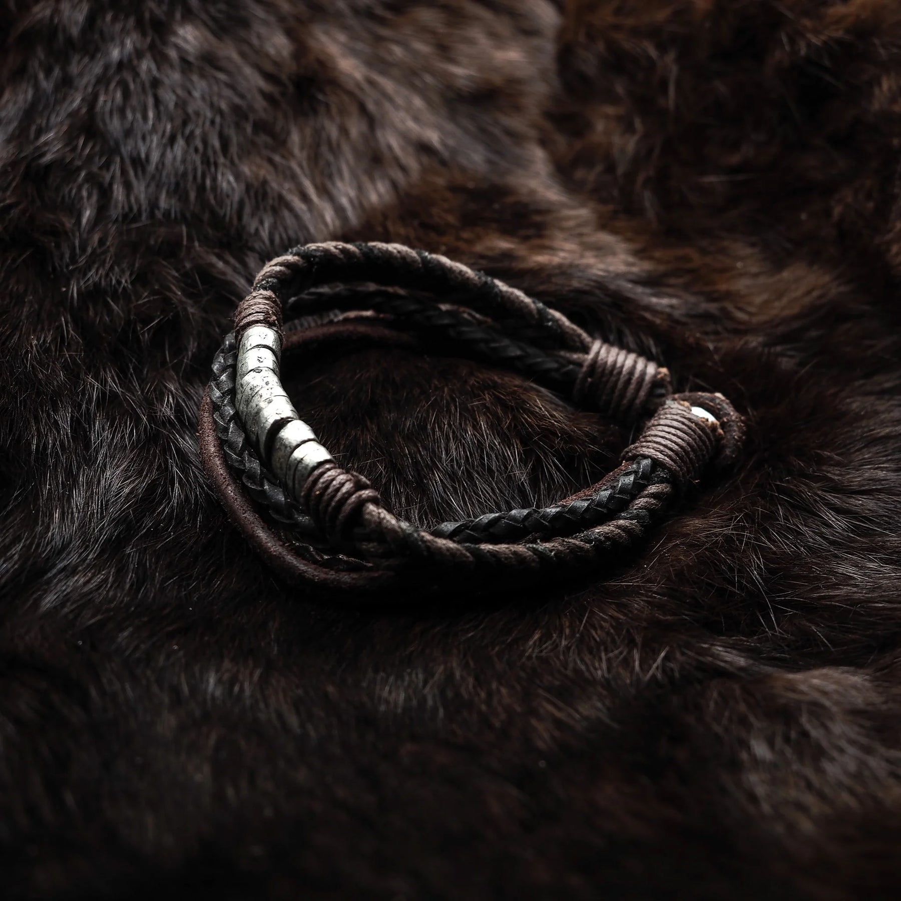 Närbild på armband i brun läder med vitsmetall omslutning på mörk textilbakgrund