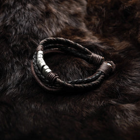Närbild på armband i brun läder med vitsmetall omslutning på mörk textilbakgrund