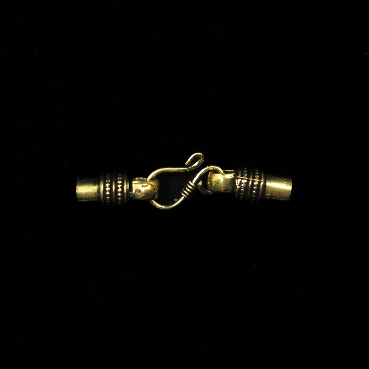 Halsbandslås i guld/mässing med S-krok och dekorerade ändhylsor mot svart bakgrund