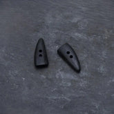 Två mörka hornknappa med naturlig färg och kornstruktur. Långsträckt form med två hål för sömnad. Visar autentisk hornmaterial, inte trä.