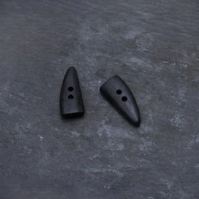 Två mörka hornknappa med naturlig färg och kornstruktur. Långsträckt form med två hål för sömnad. Visar autentisk hornmaterial, inte trä.