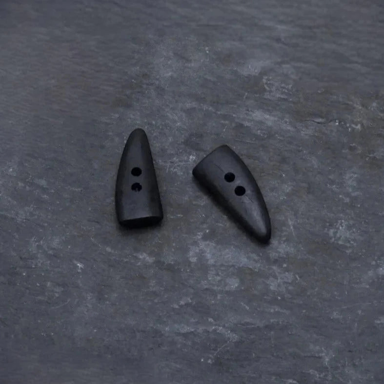 Två mörka hornknappa med naturlig färg och kornstruktur. Långsträckt form med två hål för sömnad. Visar autentisk hornmaterial, inte trä.