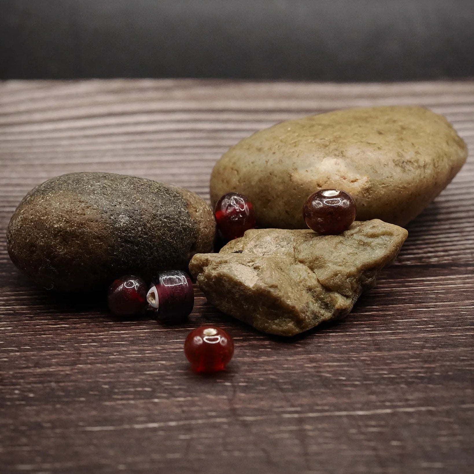 Mörkröd glaspärla, handgjord i vikingatid-stil. Djup burgundy opak glas, liten sfärisk form. Flera exemplar visar storlekskonsistens och handverkstextur. Fotograferad med arkeologisk kontext och läderkvästar.