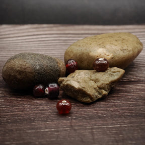 Mörkröd glaspärla, handgjord i vikingatid-stil. Djup burgundy opak glas, liten sfärisk form. Flera exemplar visar storlekskonsistens och handverkstextur. Fotograferad med arkeologisk kontext och läderkvästar.