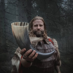 Man i vikingkostym håller stor organisk dryckeshorn (800ml) med naturlig hornstrimmning mot mörk skogsbakgrund