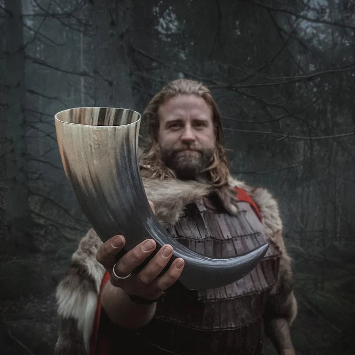 Man i vikingkostym håller stor organisk dryckeshorn (800ml) med naturlig hornstrimmning mot mörk skogsbakgrund
