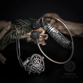 Freja gåvoset med silverpläterat mässingsarmband, hjärtanhängare med änglaklocka och sfäriska pärlor på mörk bakgrund med barrgrenar