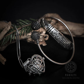 Freja gåvoset med silverpläterat mässingsarmband, hjärtanhängare med änglaklocka och sfäriska pärlor på mörk bakgrund med barrgrenar