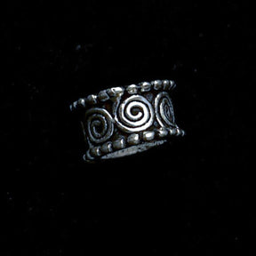 En silverfärgad hårpärla med vikingiska spiralmönster och dekorativa punkter, framställd mot mörk bakgrund. Vikingisk hårsmycke i metall.