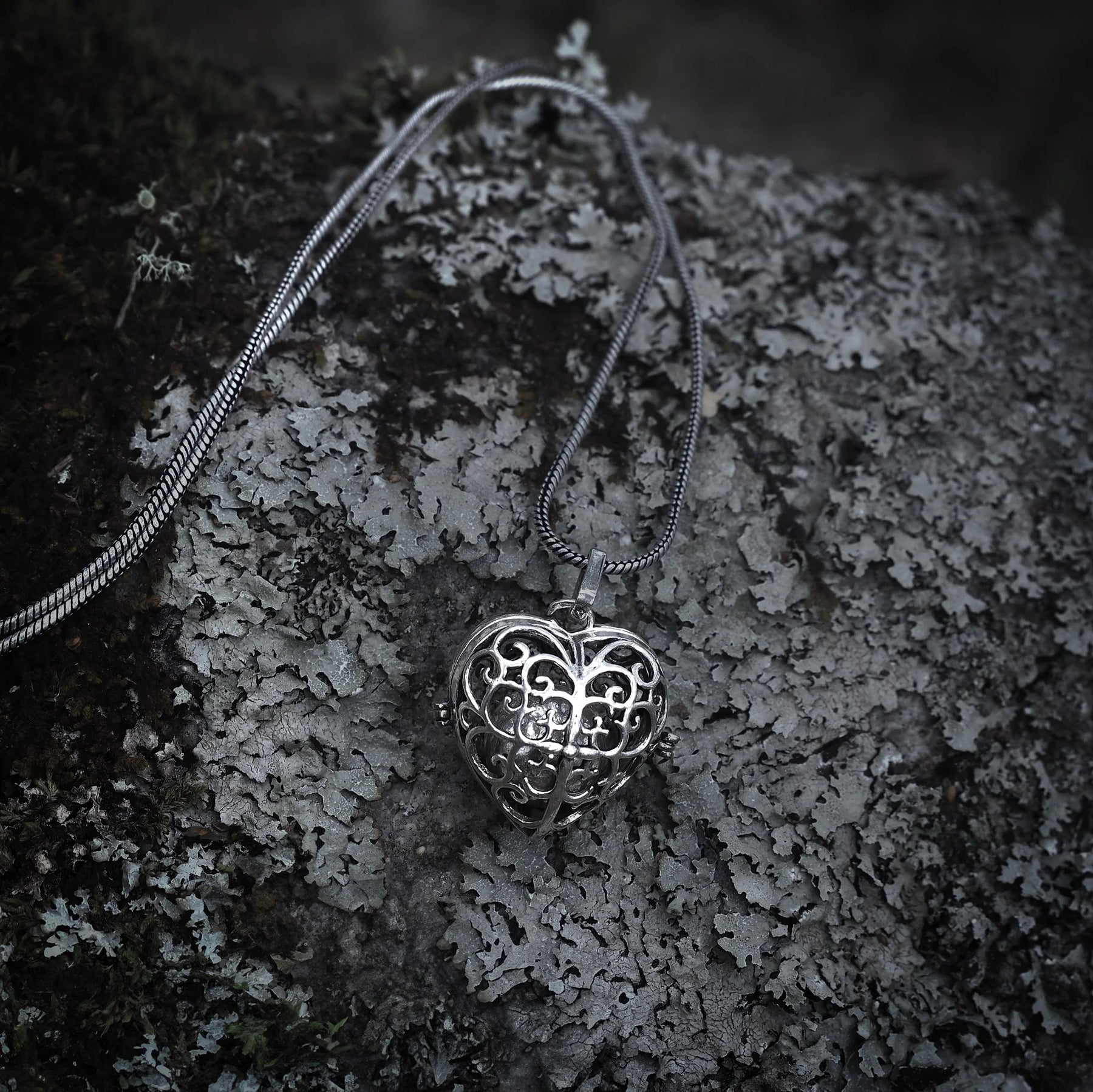 Silverpläterad hjärtformad berlock med detaljerat filigranmönster och ornamental snirkelmönster på strukturerad grå sten.
