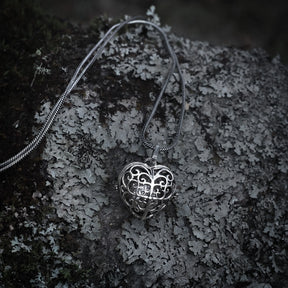 Silverpläterad hjärtformad berlock med detaljerat filigranmönster och ornamental snirkelmönster på strukturerad grå sten.