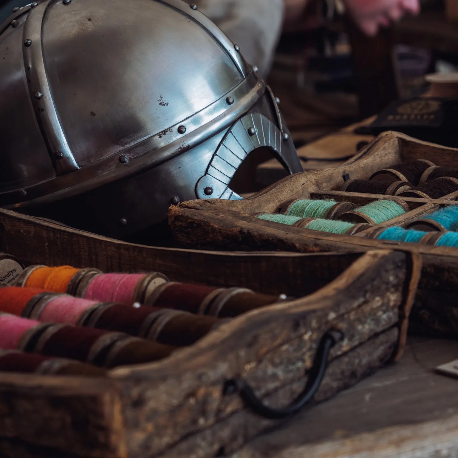 Färgglada ullgarnsspolar i trälådor med vikingahjälm, visar sortimentet av brodyrtråd i ull