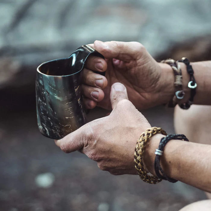 Hornmugg hållen i två händer, mörkbrunt naturhorn med handtag, praktisk användning
