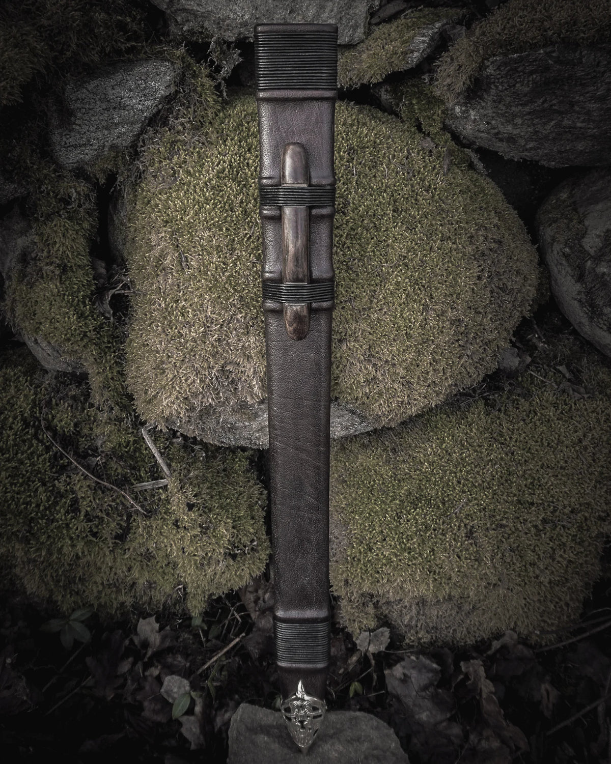 Fullängds svärdskida 'Black Ice' i svart läder med mässingsmontage, fotograferad vertikal mot naturlig bergsformation