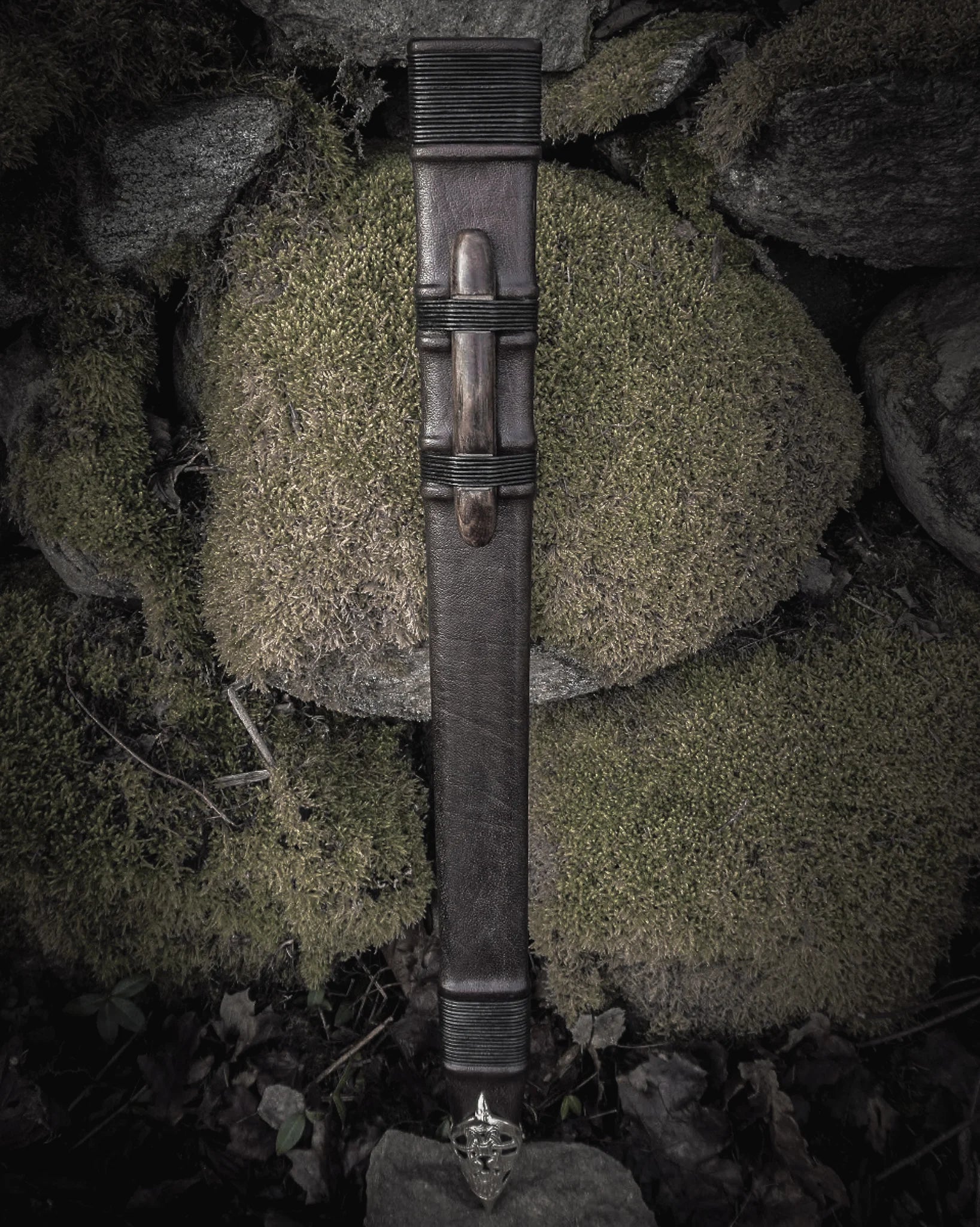 Fullängds svärdskida 'Black Ice' i svart läder med mässingsmontage, fotograferad vertikal mot naturlig bergsformation