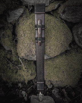 Fullängds svärdskida 'Black Ice' i svart läder med mässingsmontage, fotograferad vertikal mot naturlig bergsformation