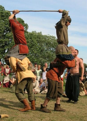 Festivalfotografi från Scandinavian games visar två människor i traditionell vikingakläder som tävlar med ett tjockt trästag held högt över deras huvuden, kämpandes för kontroll
