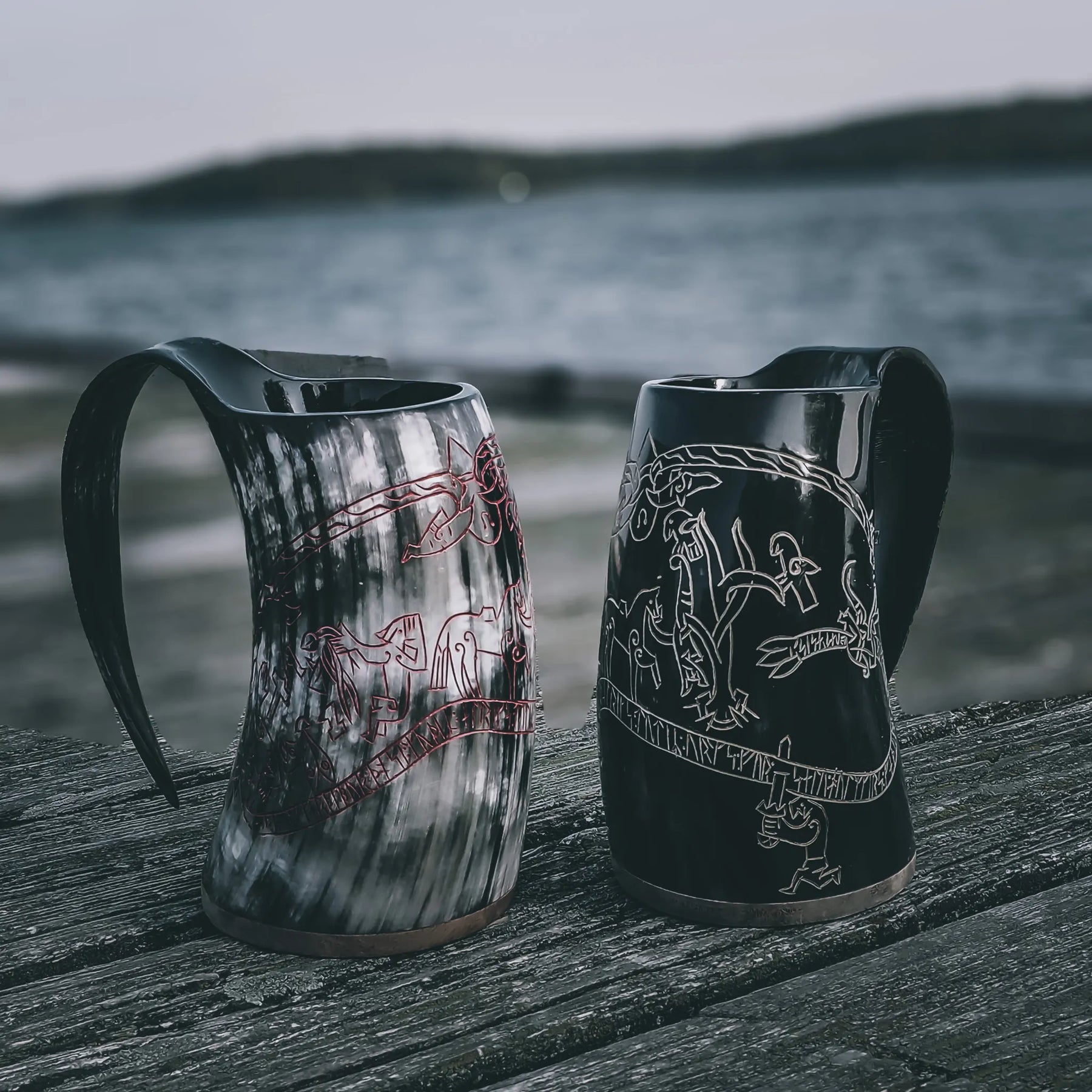Två hornmuggar med Sigurdsagan-gravering. En är naturlig hornfärg, den andra mörkblack. Båda visar fina graverade nordiska motiv och runor. Trä- och hornbottnar.