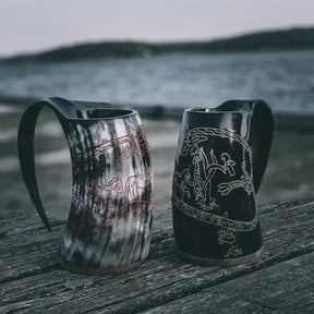 Två hornmuggar med Sigurdsagan-gravering. En är naturlig hornfärg, den andra mörkblack. Båda visar fina graverade nordiska motiv och runor. Trä- och hornbottnar.