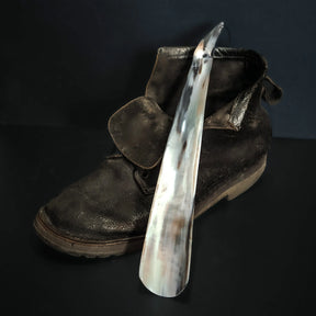 Skohorn i horn, spetsig shoe horn being used with black leather boot, demonstrating practical application
