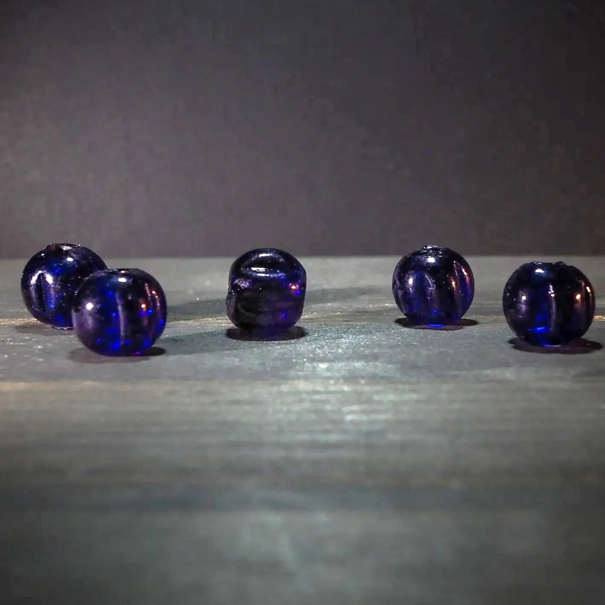 Blå melonpärlor i glas. Fyra kulor med mörkblå till violett färg. Pärlorna visar naturlig färgvariation och metalliska reflektioner. Material: glas. Användning: pärlor för smycken och armband.