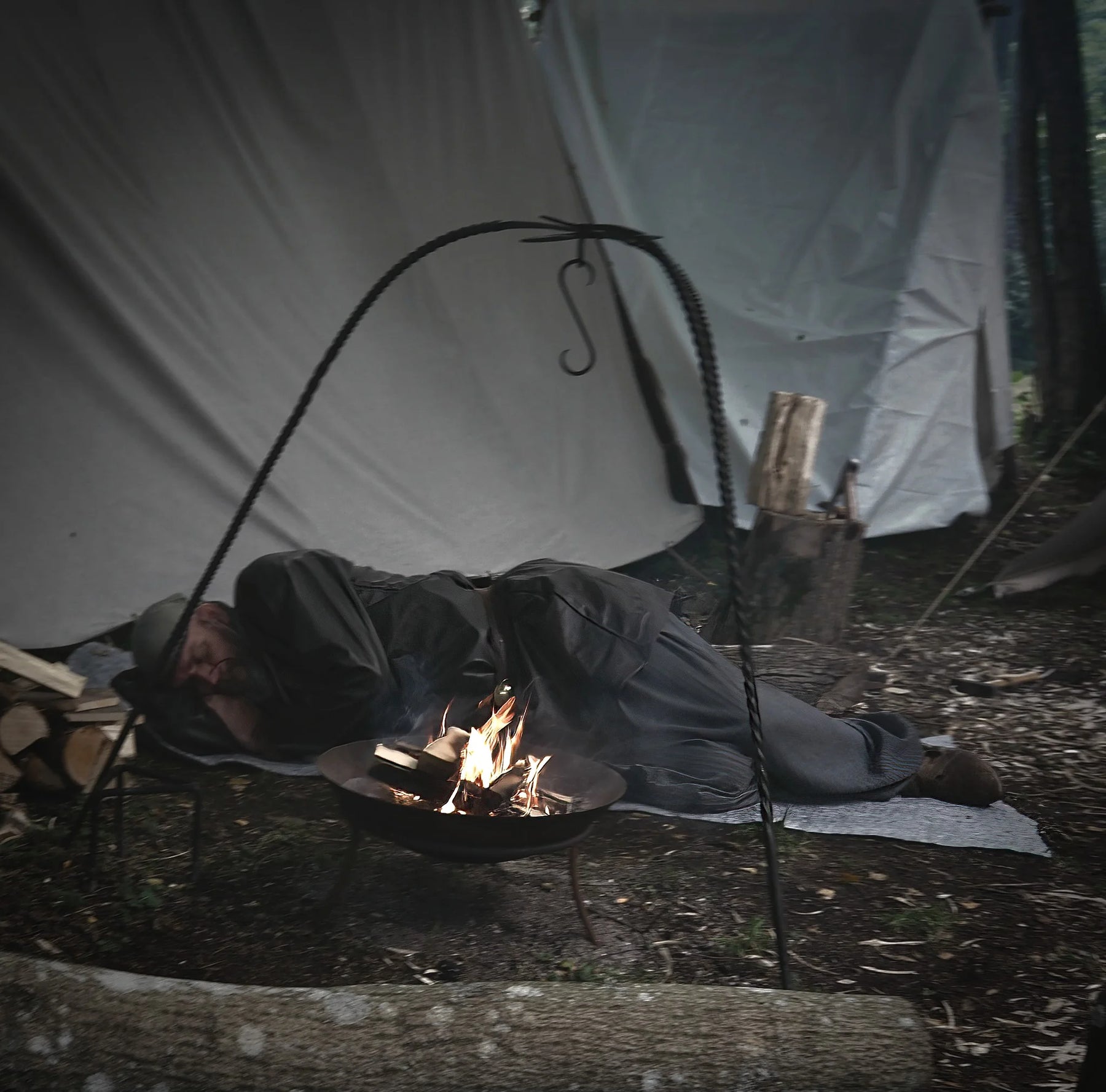 Person camping with handfelted wool blanket positioned in shelter near campfire, demonstrating outdoor adventure use