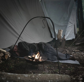 Person camping with handfelted wool blanket positioned in shelter near campfire, demonstrating outdoor adventure use