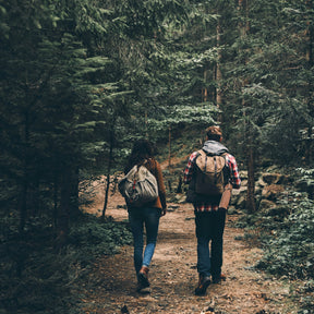 Två vandrare på skogsstig med ryggsäckar, visar visselpipan i naturlig användning under Nordic vandringsabventyrs