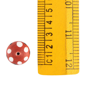 Red disc-shaped glass bead with white dot pattern, approximately 10-12mm diameter with ruler scale reference, Viking-era artifact