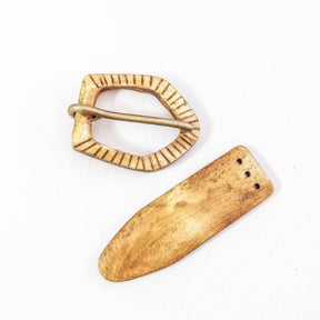 Bältesspänne i ben med två komponenter - oval spännearm med vertikalt kannelerad dekor och funktionell tungpinne, samt förlängd bältestungbit med tre fästhål på vit bakgrund