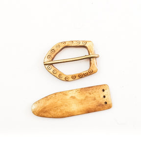 Bältesspänne i ben på vit bakgrund: D-formad spänne med prydnadsrand och mässingsnål tillsammans med bältesende med tre fästhål