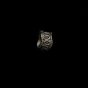 Single Elmar brass beard bead tilted to show concentric oval relief pattern and rope-trimmed edges
