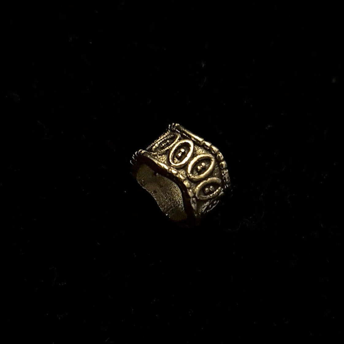 Elmar brass beard bead in three-quarter rotation displaying oval relief pattern and rope-trimmed rim edges