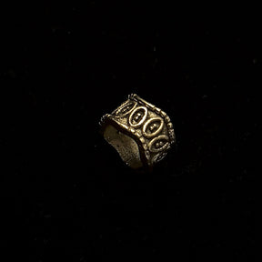 Elmar brass beard bead in three-quarter rotation displaying oval relief pattern and rope-trimmed rim edges