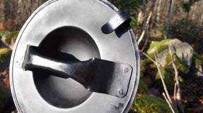 Metallbuckler i vinkel, visar inre konstruktion med konvex bål, metallremsar och rostig patina