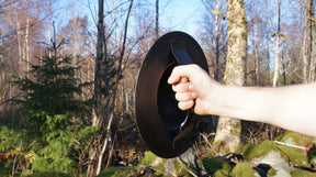 Metallbuckler sköld hållen i hand i skogsmiljö, visar bål och grå silverfärgad ram