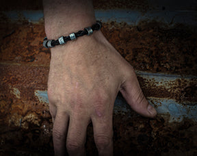Vikingaarmbandet bärat på mans handled mot industriell rostmetall bakgrund med blå och rostiga patina, visar den flätade lädern och metallkulorna i daglig användning.