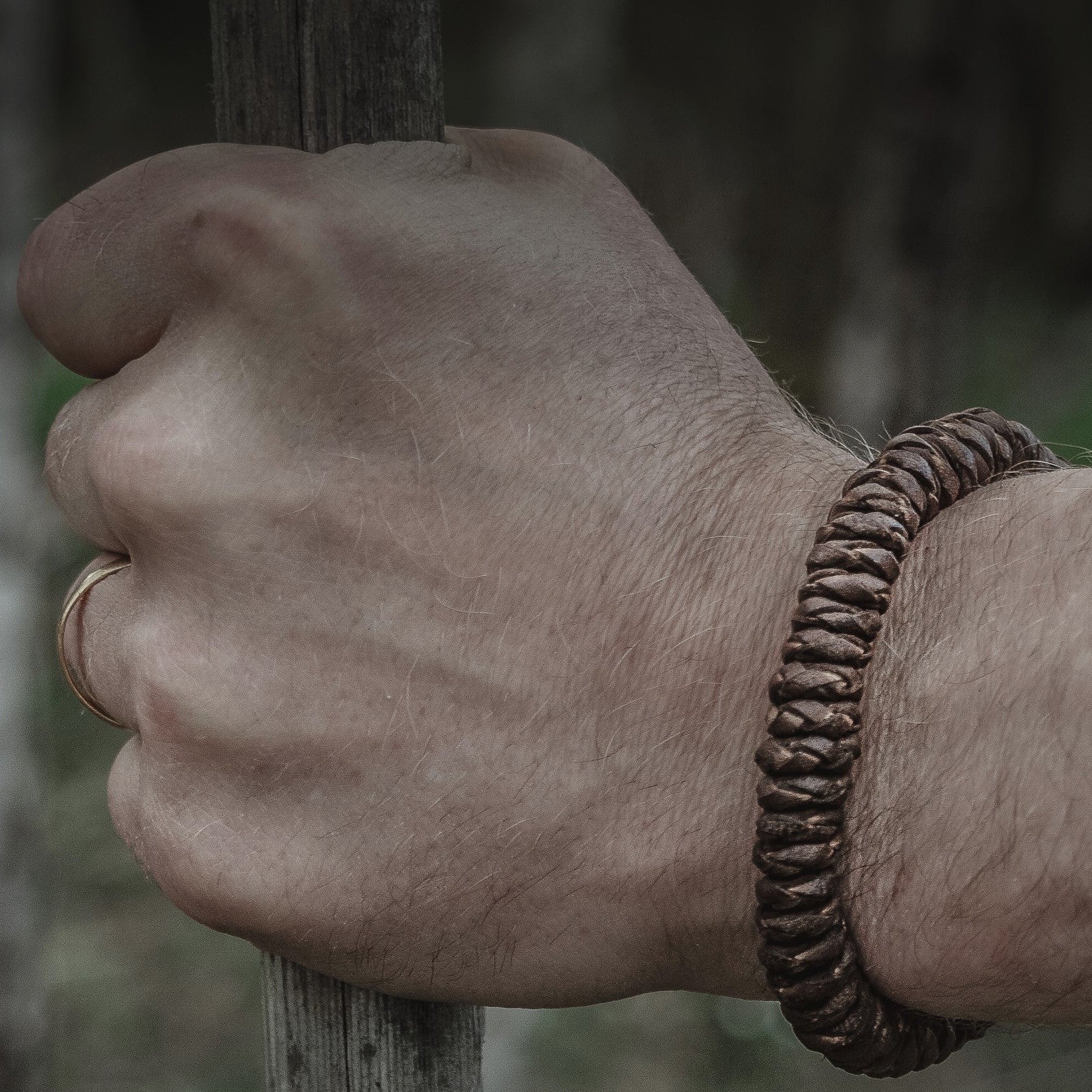 Brunt brokk-armband på en man's näve mot trä-bakgrund. Visar flätningen från nära håll och metallknappsslutningen.