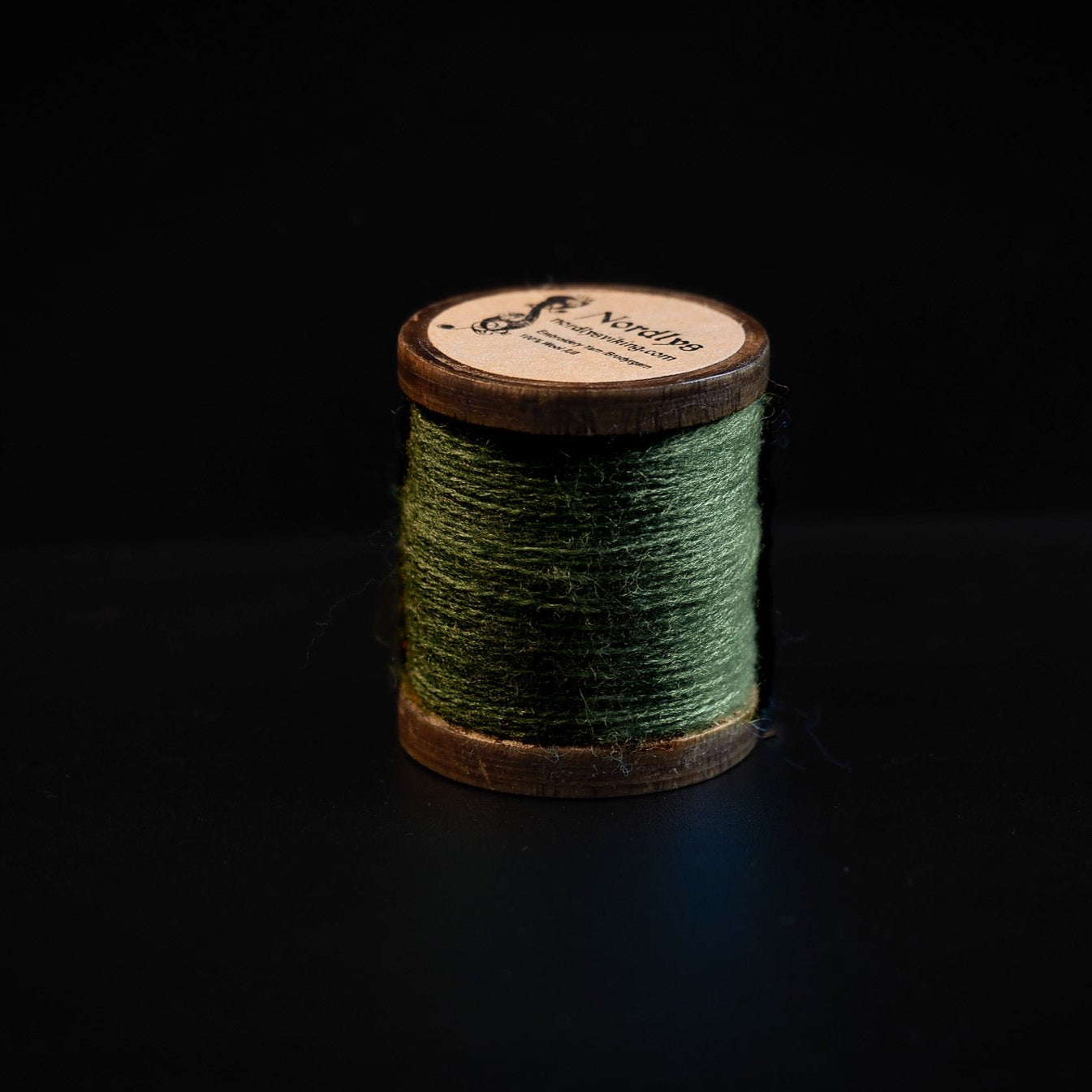Green embroidery thread in 100% wool on wooden spool with Nordlys branding, photographed against dark background to show thread texture and color